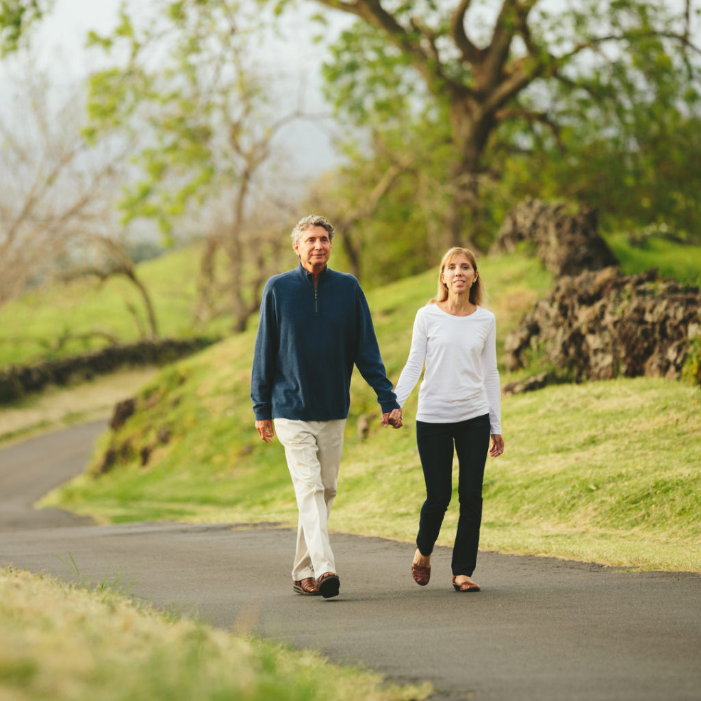 Middle aged couple walking through woods on road holding hands