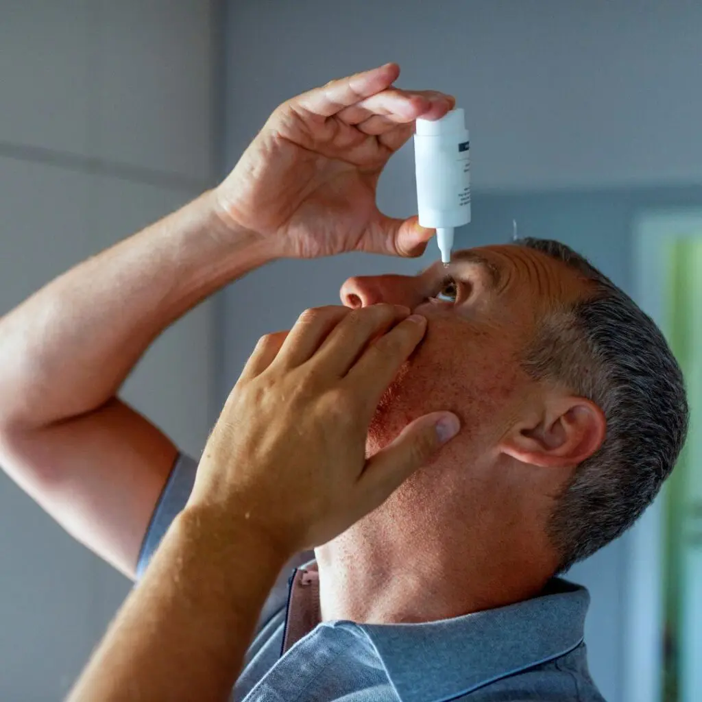stock image of middle aged man putting eye drops into his eyes to treat dry eye symptoms