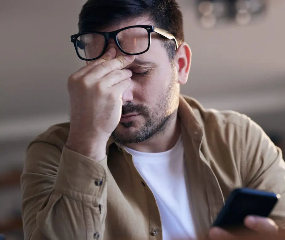 Young man having a headache while using smart phone