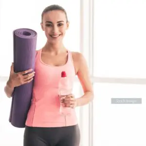 Lady standing in gym wear holding yoga mat and water bottle