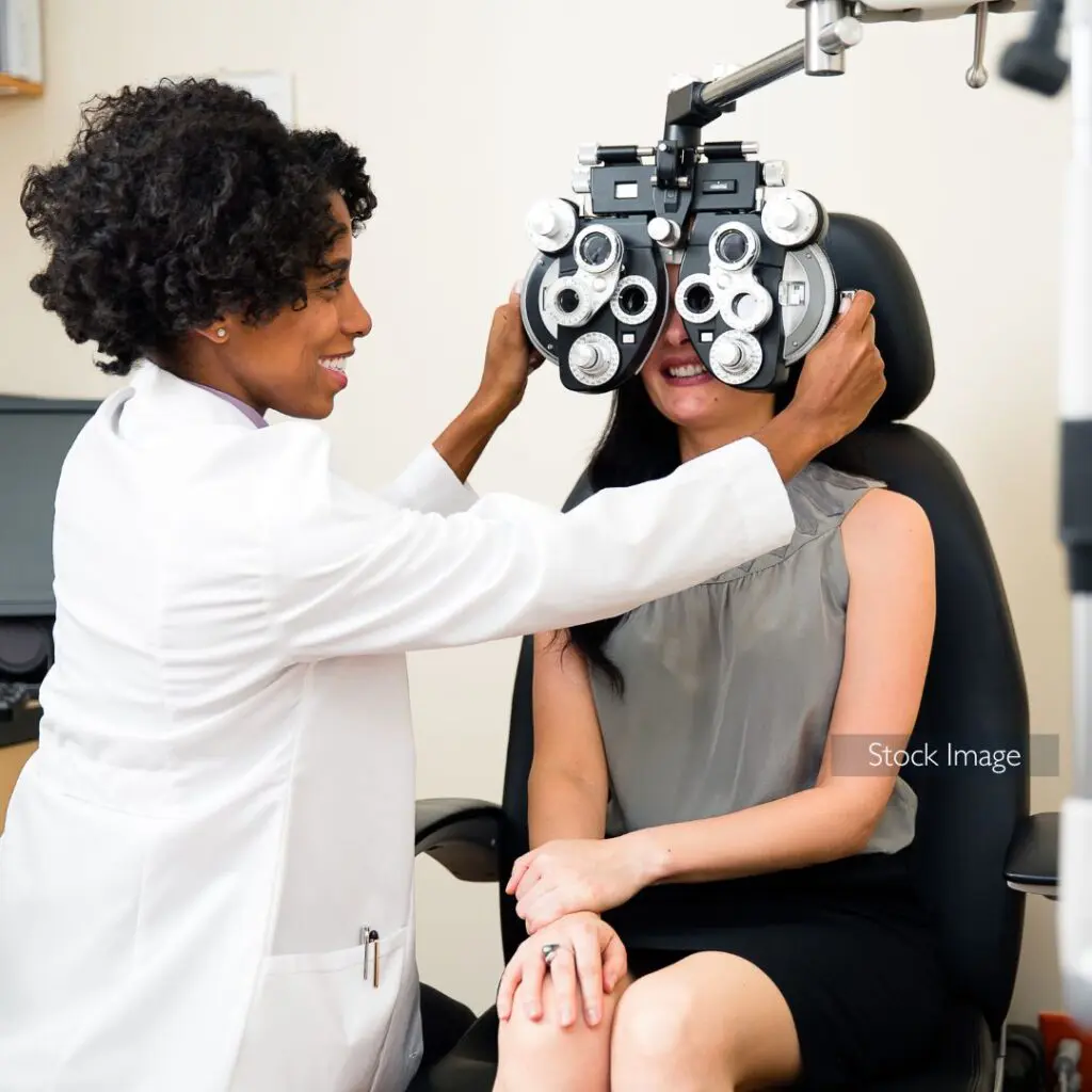 Centre for Sight stock image blog post Eye Exams: When, Why and Where lady optometrist adjusting testing machine for lady patient wearing black skirt and grey top uniform