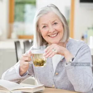 Elderly lady with grey hair smiling and she sits at the table with herbal tea grey jumper writing down in her diary stock image for patient story