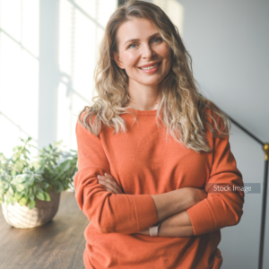 Lady standing in her house smiling wearing orange jumper
