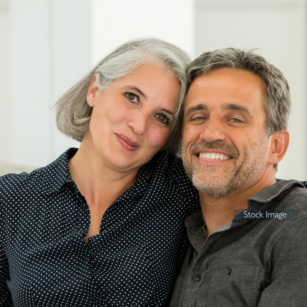 Lady and man cuddling on sofa in dark coloured shirts smiling