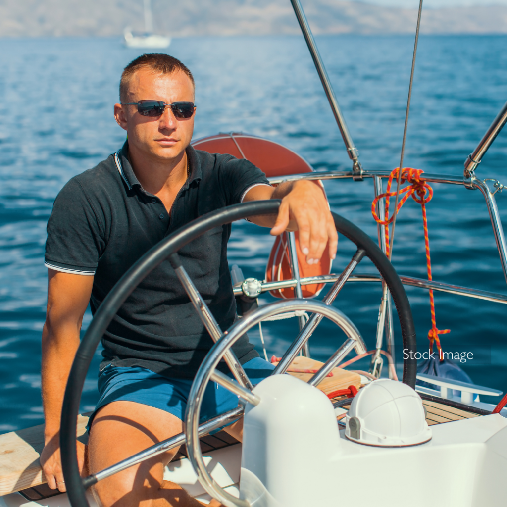 Man on boat in the ocean wearing sunglasses driving the boat