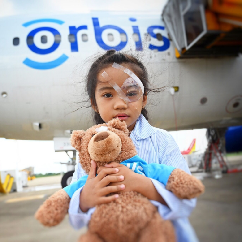 Orbis International Child holding teddy bear in front of a plane