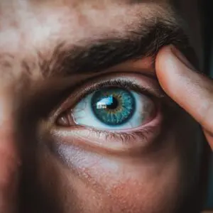Man with blue eyes holding his finger on eyelid pushing up dark eyebrow