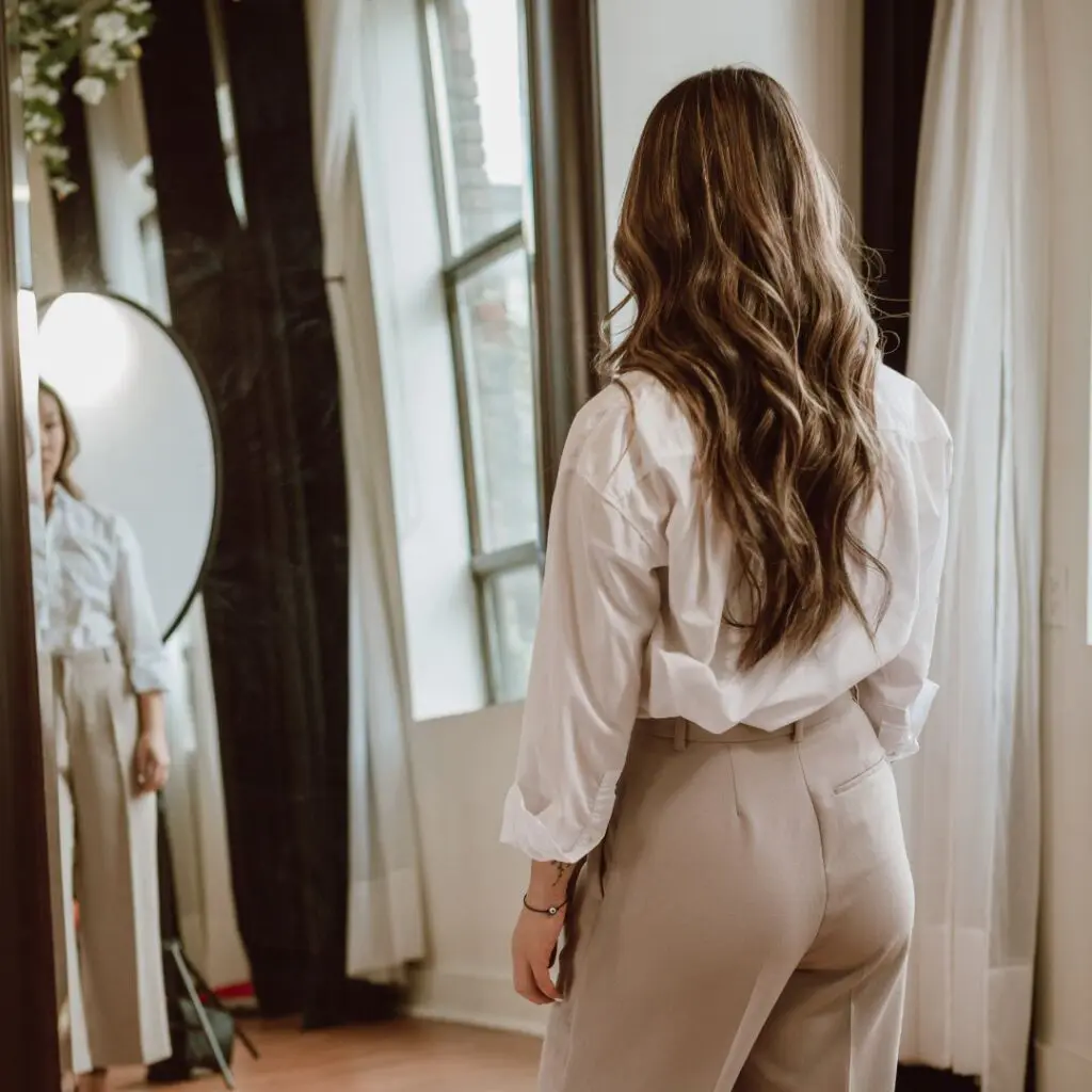 Centre for Sight see clearly live confidently stock image woman with medium length brown hair looking in mirror admiring outfit trousers and shirt