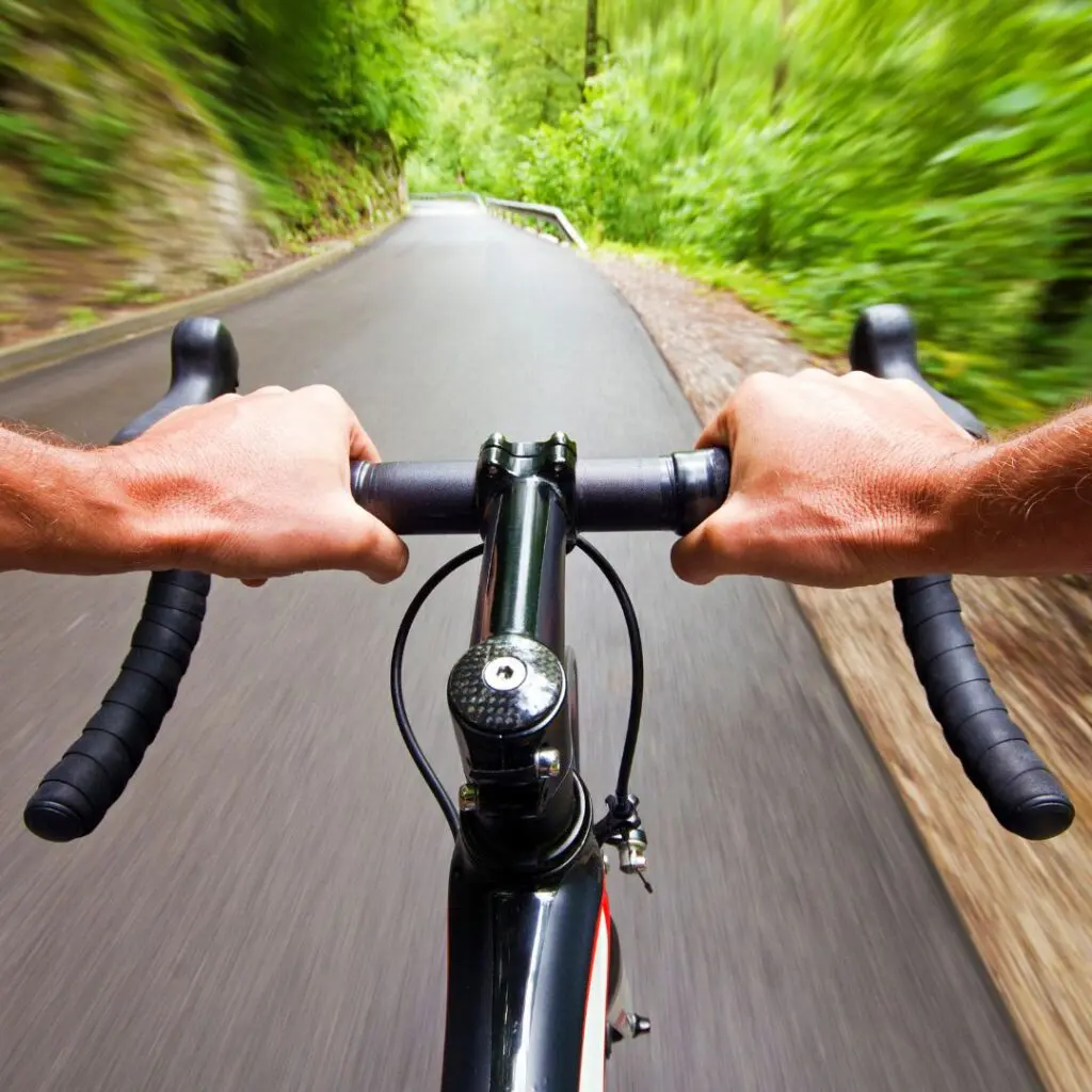 Centre for Sight stock image for vision correction man's hands on the handlebars of a bike riding through wooded area on road