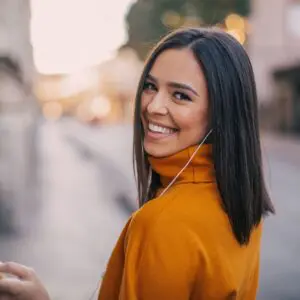 Centre for Sight dark hair short hair orange jumper woman female wearing headphones in street holding mobile phone