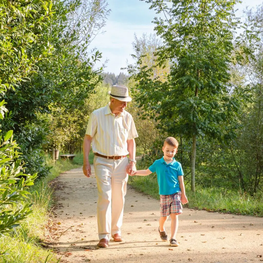 An elderly man, who recently had refractive cataract surgery at Centre for Sight, walks hand-in-hand with a young boy along a sunlit, tree-lined park path. Both are smiling, enjoying the pleasant weather and vibrant greenery around them.