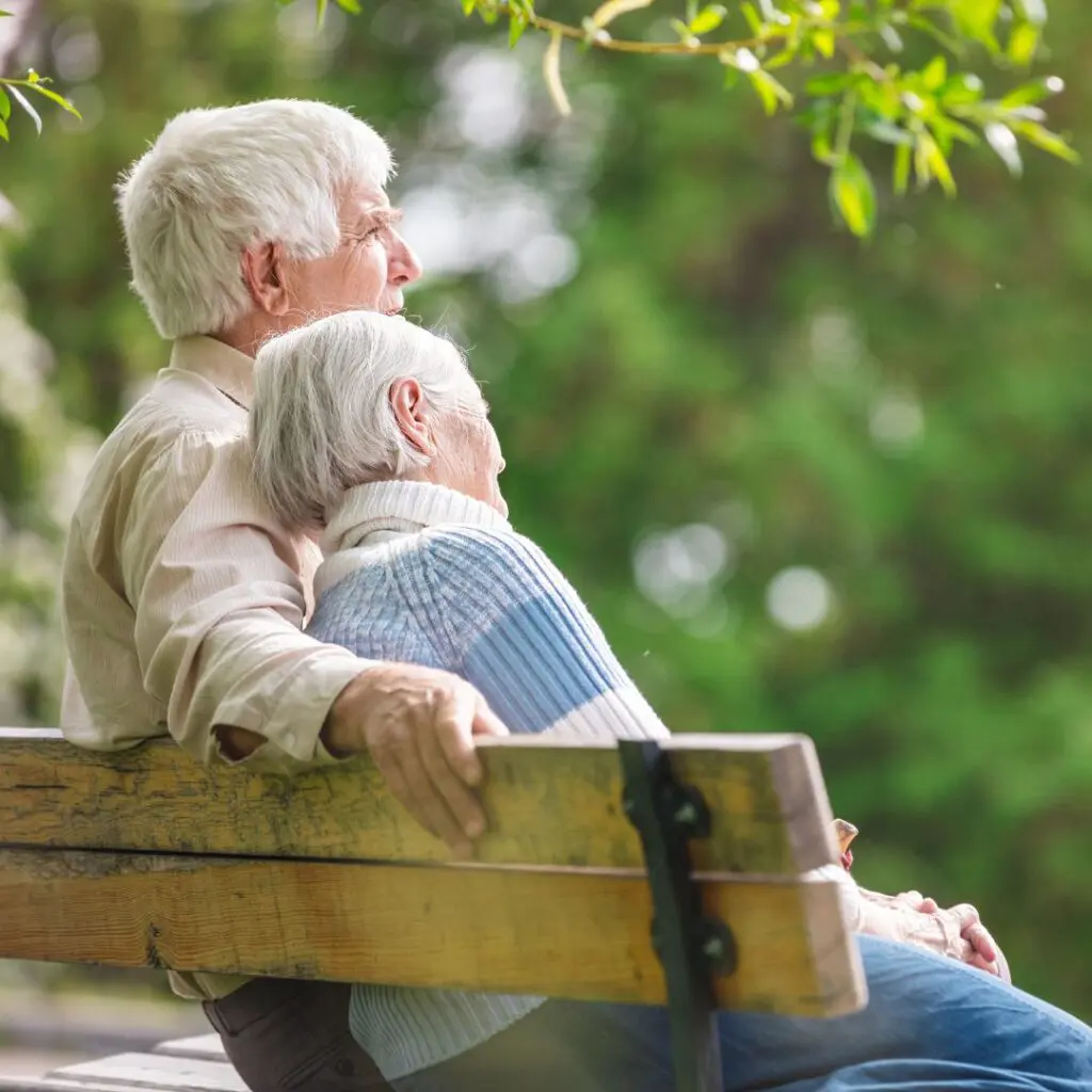 Centre for Sight elderly patients sitting on a bench in a park outside grey hair cuddling jeans and a jumper elderly couple male female