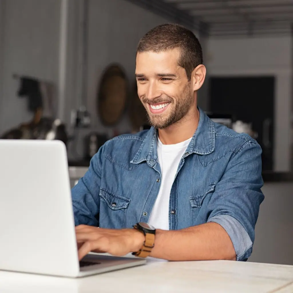 Centre for Sight youn man with blue shirt sitting at desk in kitchen using laptop researching smiling laser eye surgery blog stock image can I have laser eye surgery with astigmatism