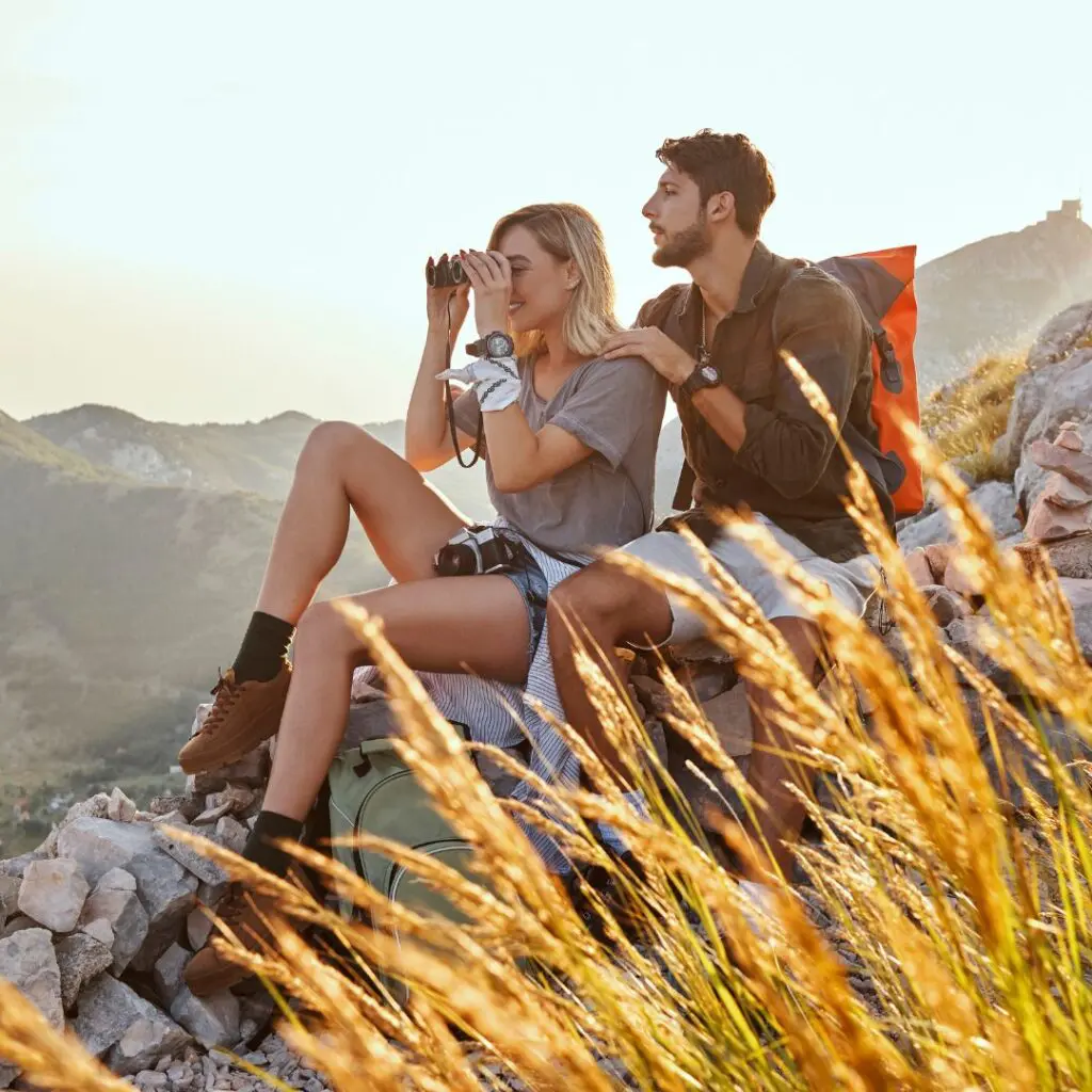 Centre for Sight young couple sitting on rock looking through binoculars after laser eye surgery