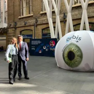 Couple posing in front of large Orbis eye installation, promoting eye health awareness for World Sight Day 2025.
