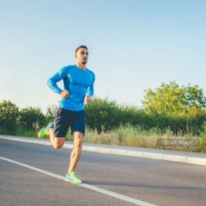 Man on running track in the summer trees around in a blue running top and shorts