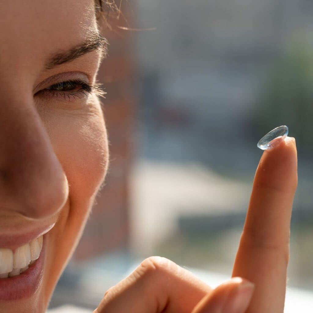 Lady standing by window smiling as she puts in contact lens balanced on finger for blog post Centre for Sight Contact Lenses Tips and Safety