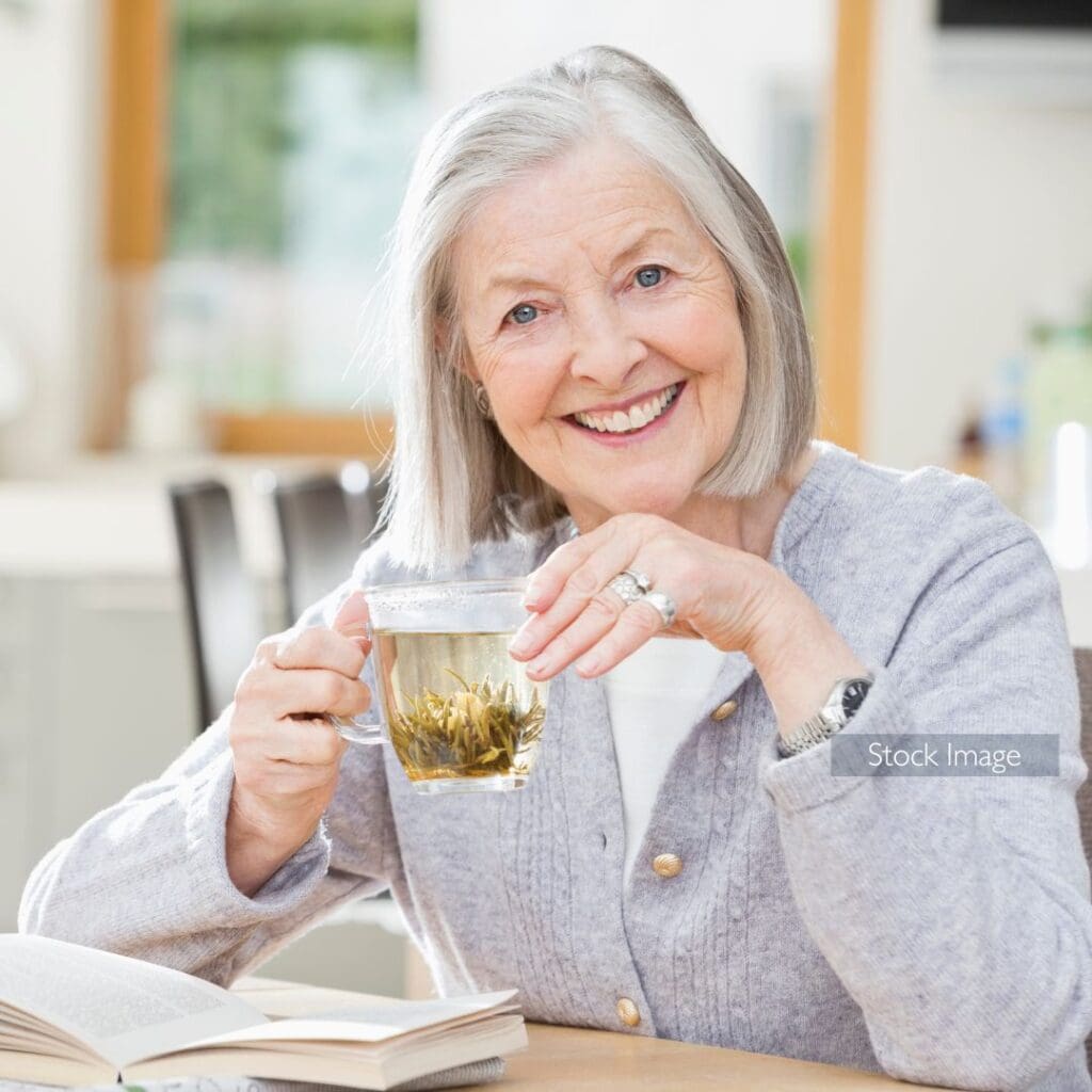 Elderly lady with grey hair smiling and she sits at the table with herbal tea grey jumper writing down in her diary stock image for patient story