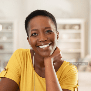 Lady with short dark hair wearing yellow top leaning her chin on her hand sitting down smiling