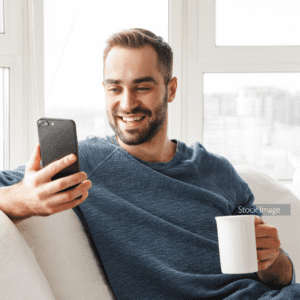 Young man sat on the sofa with a coffee looking at his phone grey shirt and brunette hair