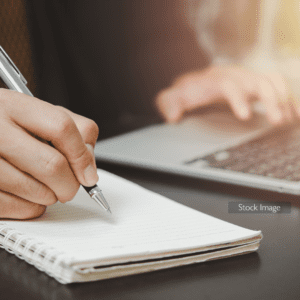 Man writing on a notepad with a pen and laptop