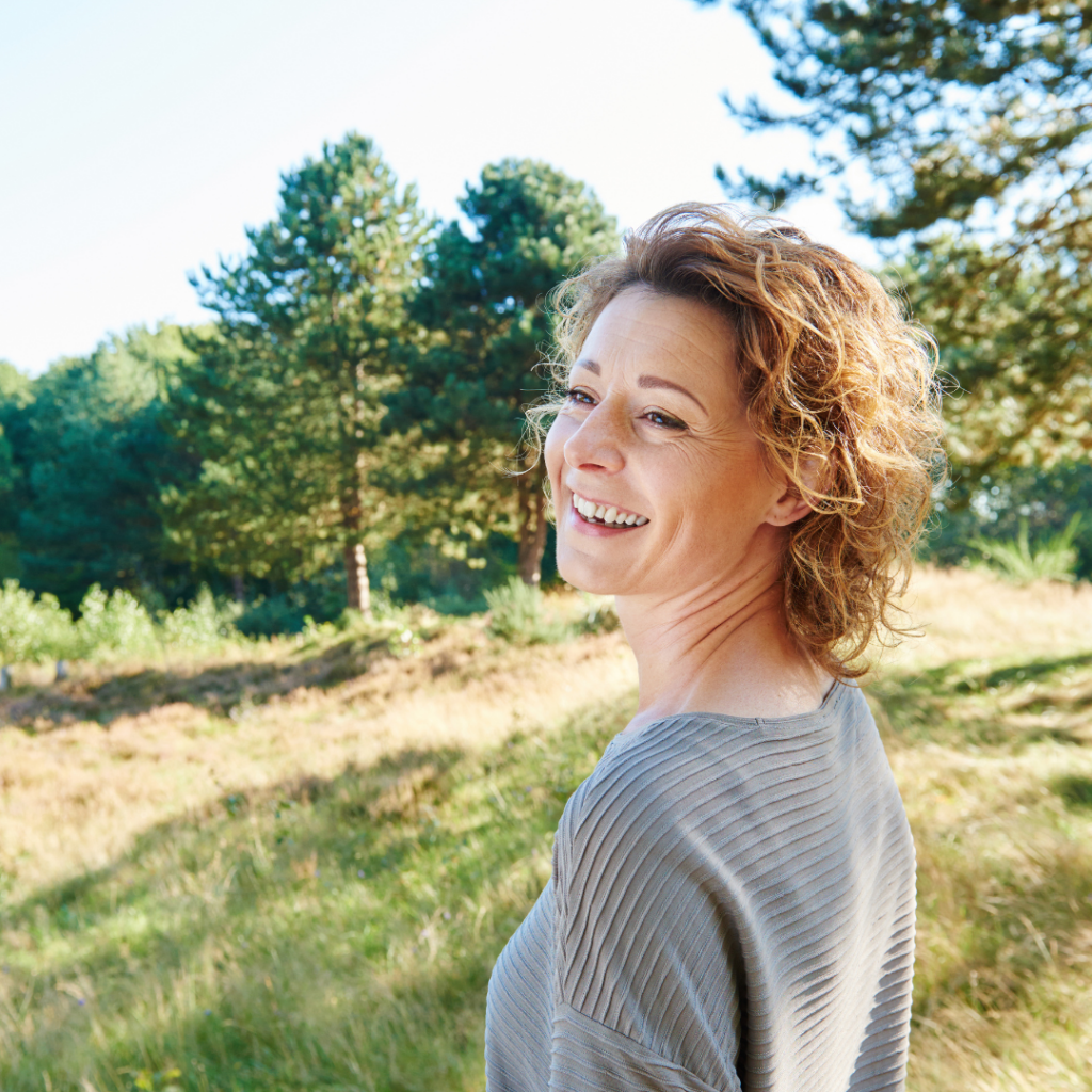 Middle aged lady walking on British forest terrain smiling with trees around her