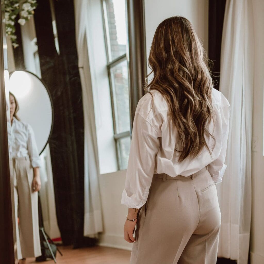 Centre for Sight see clearly live confidently stock image woman with medium length brown hair looking in mirror admiring outfit trousers and shirt