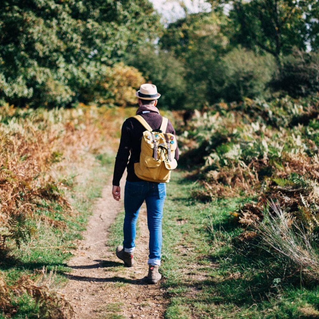 Centre for Sight older man wearing hat backpack jeans walking along in forest in nature