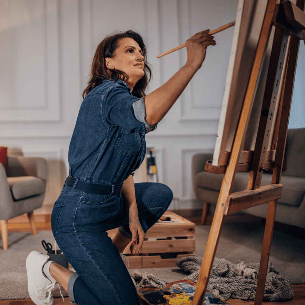 Centre for Sight lady in denim overalls painting on easel after vision correction stock image dark hair artsy
