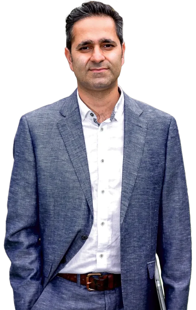 2RT Rejuvenation 6 A man in a blue suit and white shirt stands facing the camera, holding a laptop by his side. He has short dark hair and a slight smile, exemplifying the professional look associated with 2rt style. The background is plain and white.